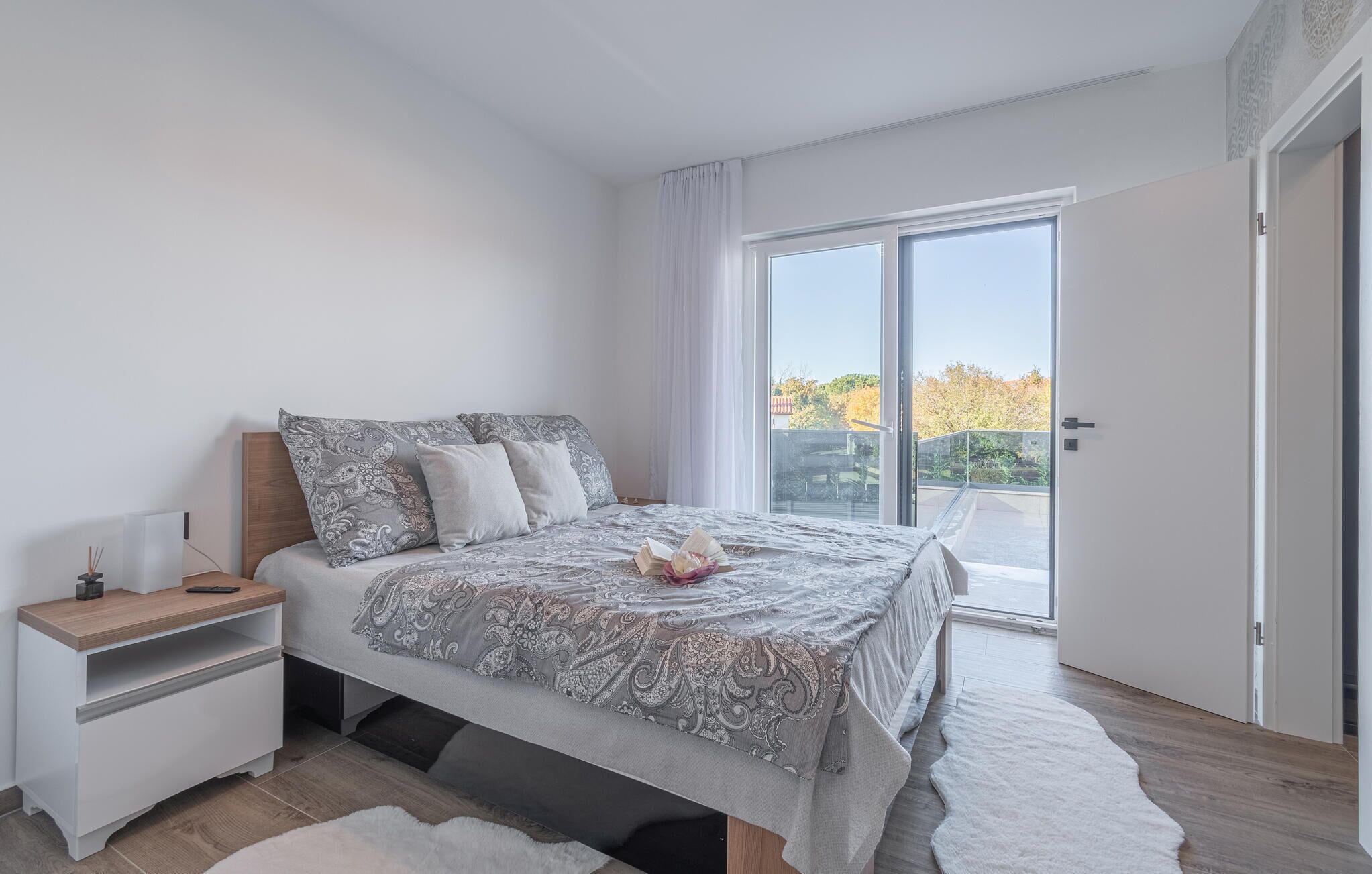 Une chambre moderne avec un grand lit, une table de chevet et une vue sur l’extérieur grâce à une porte-fenêtre coulissante.