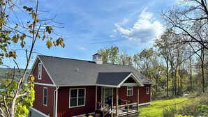 Ein rotes Haus mit Veranda, umgeben von einer Rasenfläche und Bäumen.