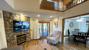 Ein Wohnzimmer mit Steinwand, Flachbildfernseher, Kamin, Essbereich mit Tisch und Stühlen sowie einer Treppe.