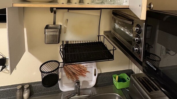 Een keuken met een spoelbak, fornuis en planken met servies en kopjes.