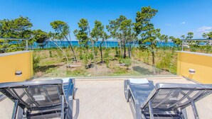 En balkong med två solstolar, utsikt över havet och en rad träd.