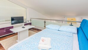 Ett modernt hotellrum med en säng, en TV, ett skrivbord och en balkong.
