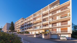 Een meerlaags woongebouw met balkons, een overdekte parkeerplaats en een auto ervoor.