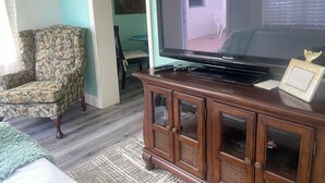 Una sala de estar con televisor, un sillón floral, un aparador de madera y obras de arte en las paredes.