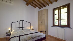 A bedroom with a metal bed frame, a bedside lamp, a wooden wardrobe, a window with a view, and a radiator. - Pet friendly home in Fauglia with WiFi (Fauglia)