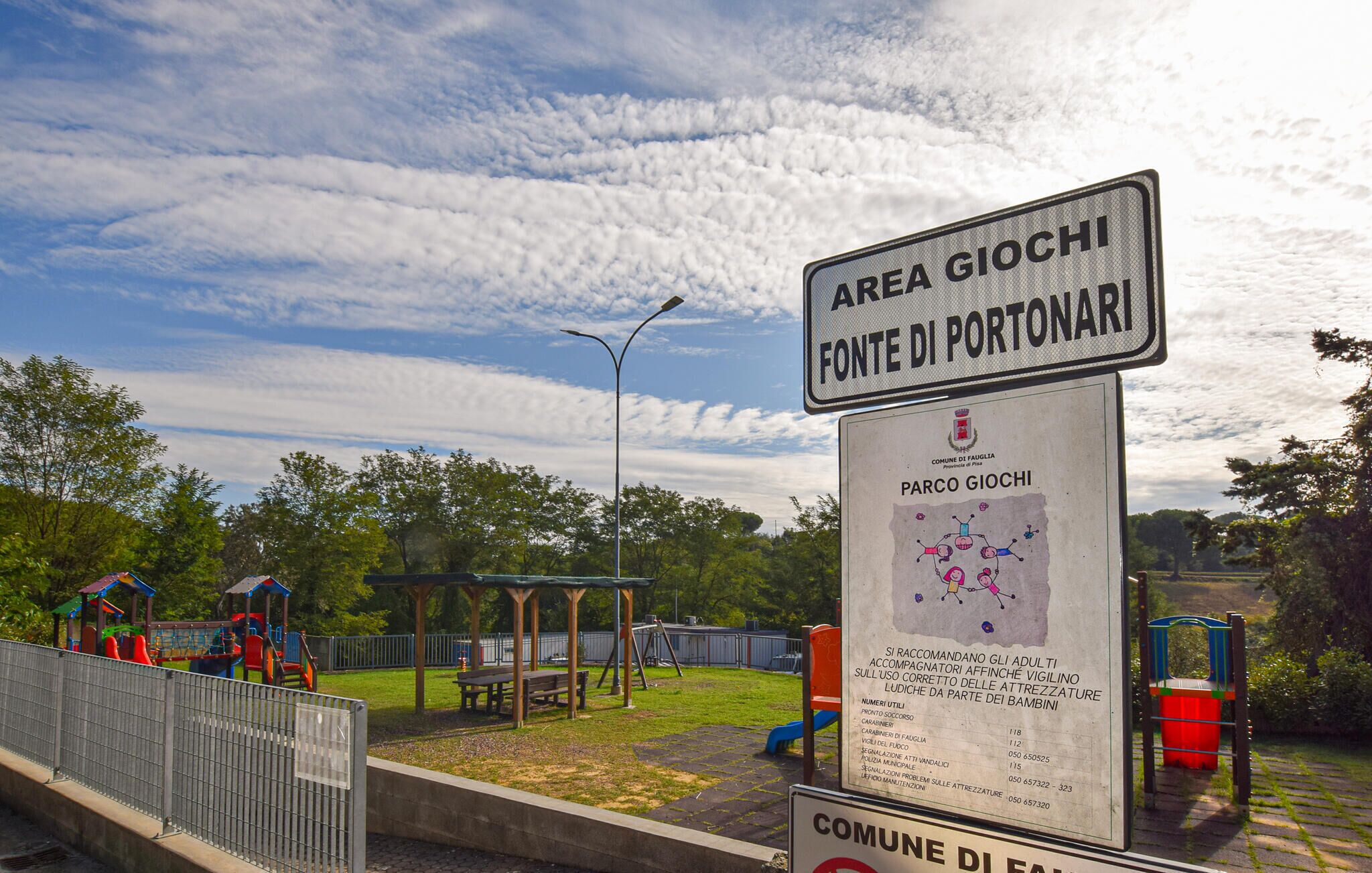 Un panneau indiquant « Aire de jeux Giochi Fonte di Portonari », avec un terrain de jeux en arrière-plan.