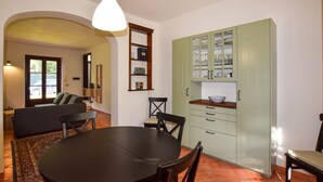 A dining area with a round table and chairs, a light green cabinet with glass doors, and a hanging light fixture. - Pet friendly home in Fauglia with WiFi (Fauglia)