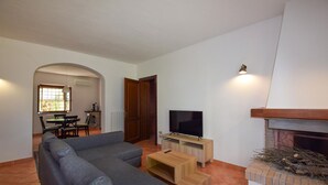 A living room with a sectional sofa, a TV on a wooden stand, a fireplace, and a dining area in the background. - Pet friendly home in Fauglia with WiFi (Fauglia)