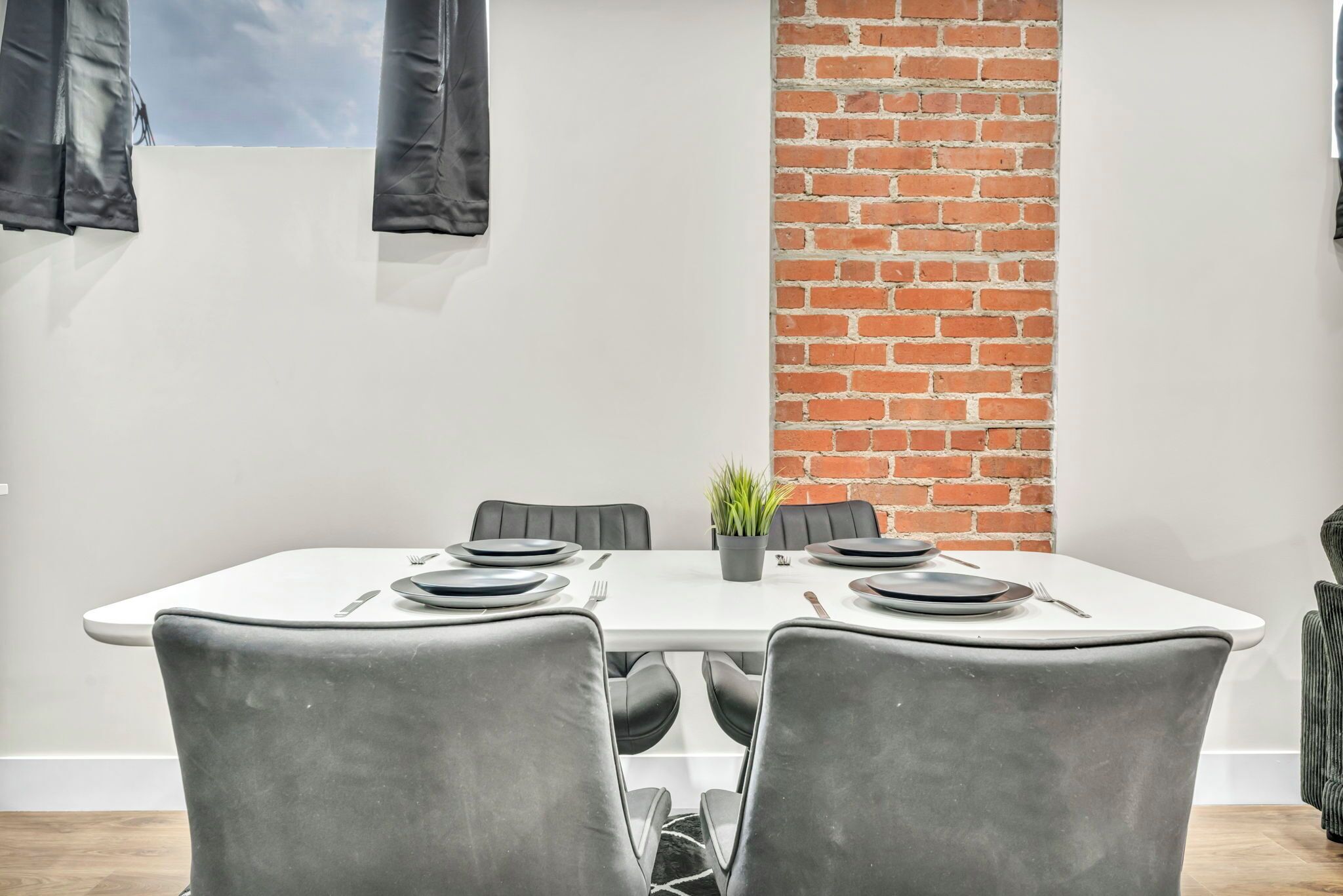 A dining area with a white table, black chairs, and a brick wall.