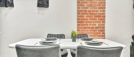 A dining area with a white table, black chairs, and a brick wall.