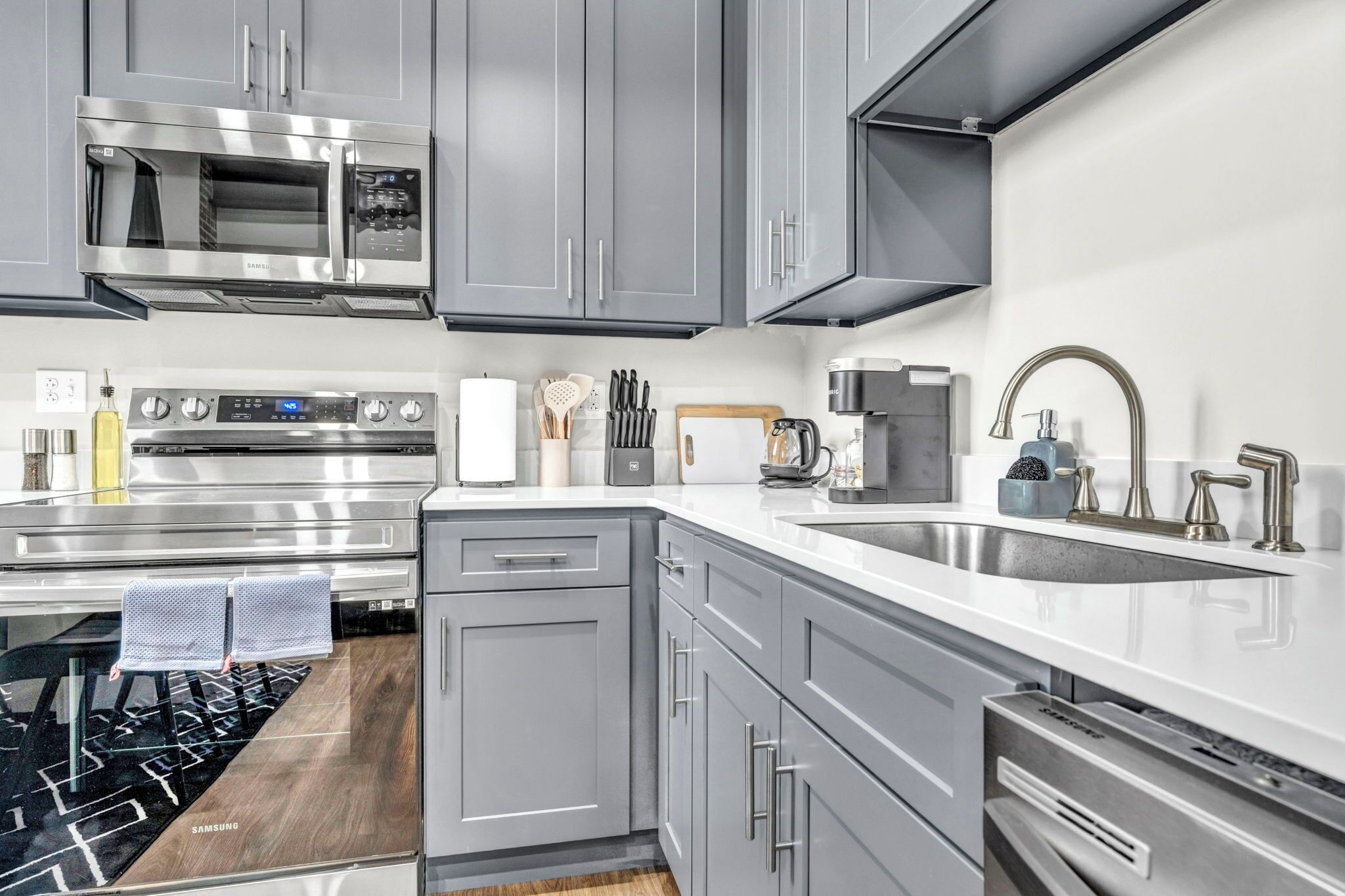 A modern kitchen with grey cabinets, stainless steel appliances, and a white countertop.