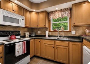 Une cuisine avec des meubles en bois, un four à micro-ondes, une cuisinière et une fenêtre donnant sur un paysage verdoyant.