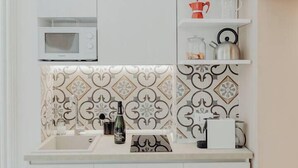 Et køkken med mikroovn, hylder med køkkenudstyr, vask og mønstrede backsplash-fliser.