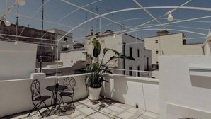 En tagterrasse med hvid gelænder, en potteplante og to metalstole.