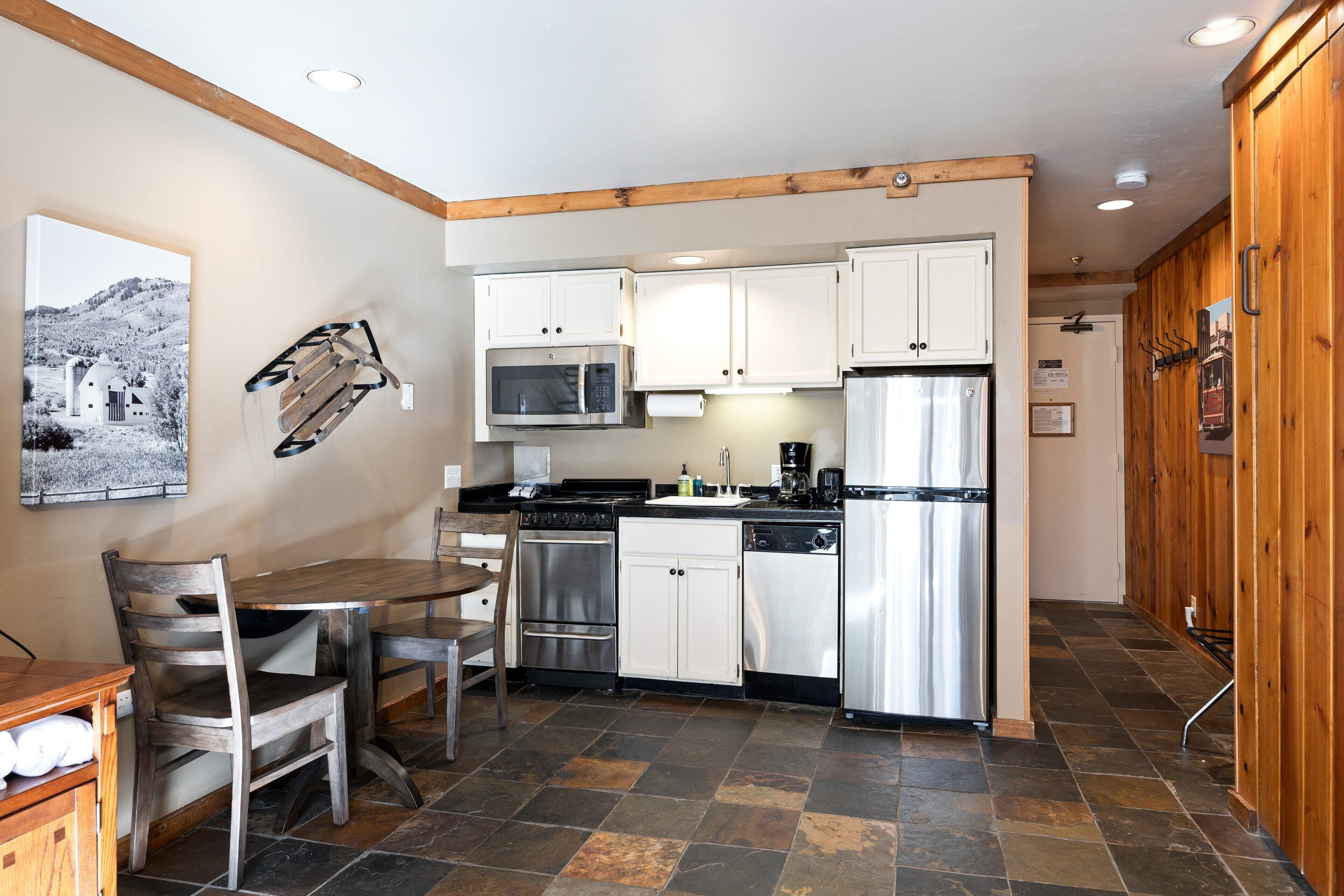 A compact kitchen with white cabinets, stainless steel appliances, and a wooden dining table with chairs.