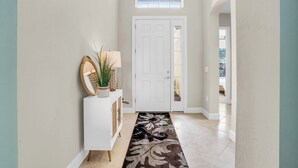 Un pasillo con una puerta blanca, una planta en maceta y un tapete decorativo.
