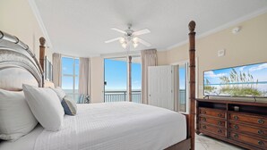 A four-poster bed with a wooden headboard, a ceiling fan, and a large flat-screen TV on a wooden dresser. - Palacio 902 | Beachfront & Resort Amenities | My Beach Getaways (Pensacola)