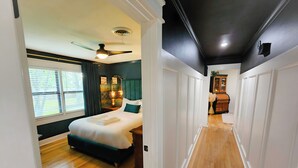 A hotel room with a bed, a ceiling fan, a nightstand, a lamp, and a view of the hallway. - The BlueStone-Stylish 3BR in Central Abilene (Abilene)