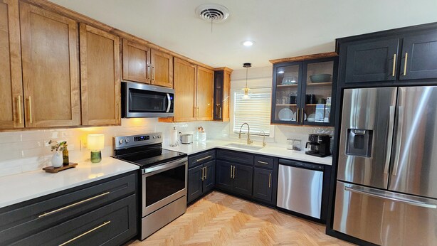 A modern kitchen with wooden cabinets, stainless steel appliances, and a herringbone wood floor. - The BlueStone-Stylish 3BR in Central Abilene (Abilene)