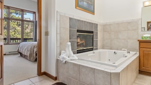 Un baño con una bañera grande, una chimenea y vistas a un dormitorio con cama y ventana.