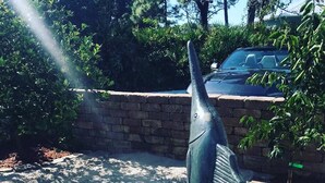 Eine Fischskulptur in einem Garten mit einer Ziegelmauer und einem Auto im Hintergrund.