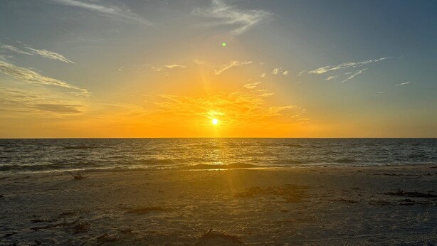 Ein Strand bei Sonnenuntergang, der eine Silhouette der Sonne am Horizont wirft.