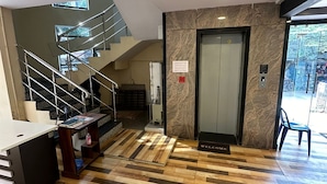 A hotel lobby with a staircase, reception desk, and a reception area with a marble wall and elevator. - Hotel Star Inn (Visakhapatnam)
