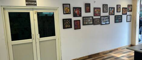 A room with a kitchen sign, a wooden floor, and a wall with framed pictures.