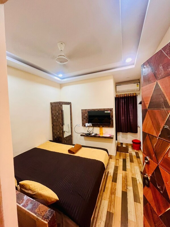 Quarto de hotel com cama, televisão fixada na parede, guarda-roupa e casa de banho com chuveiro e sanita.