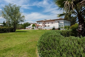 A large, white building with a red-tiled roof, surrounded by well-maintained lawns and trees. - Villa Yvonne by MMega (Signa)