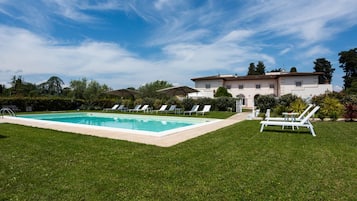 A swimming pool with lounge chairs, a well-maintained lawn, and a large building in the background.
