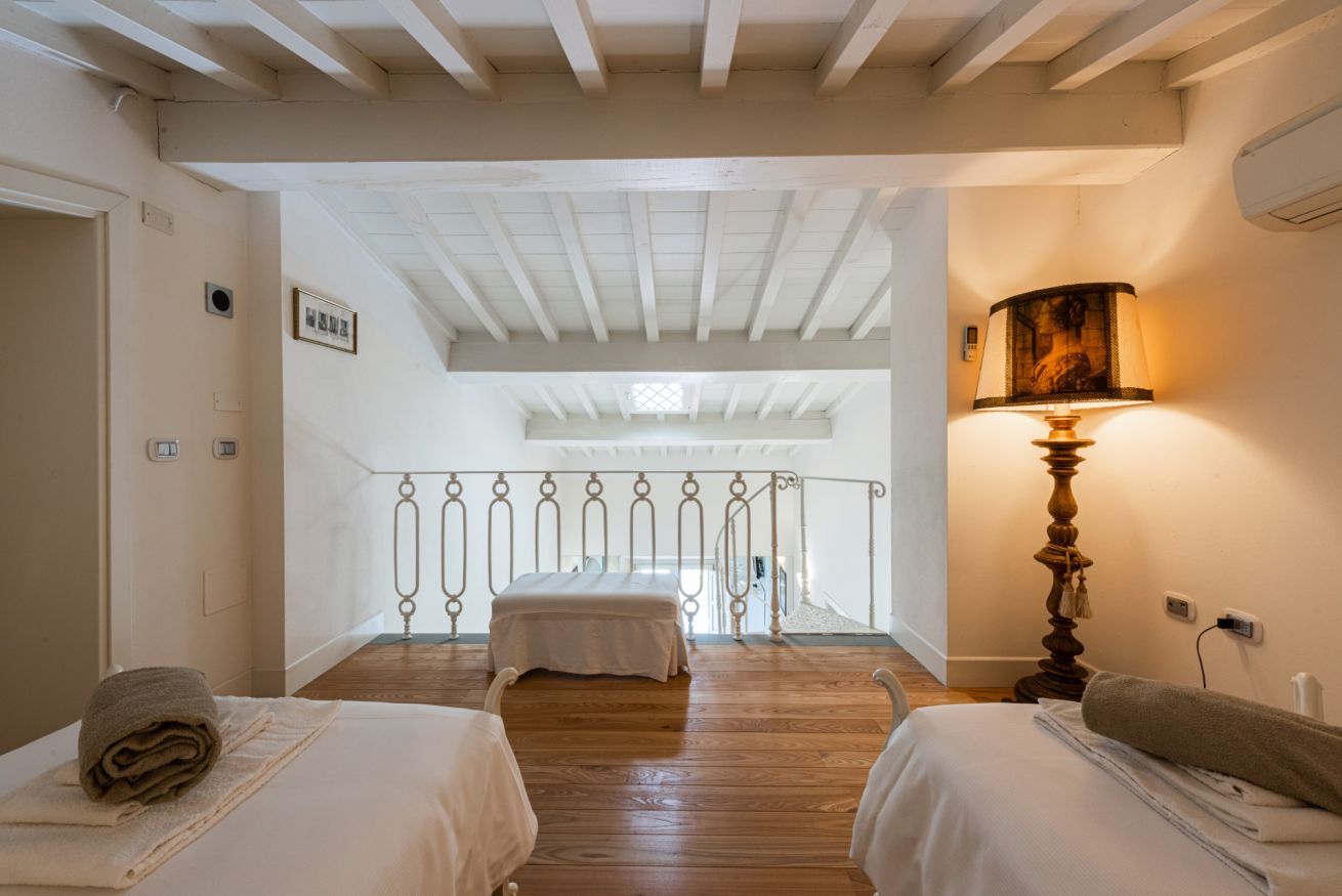 A hotel room with two beds, a wooden floor, a staircase, and a lamp.