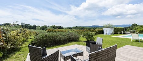 Um pátio externo com móveis de vime, piscina e vista para o campo.