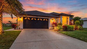 A residential house with a garage, a driveway, and well-maintained landscaping. - Captivating Paradise, Pool Table, Tiki Hut, Kayak - Cape Sunset Villa - Roelens (Cape Coral)