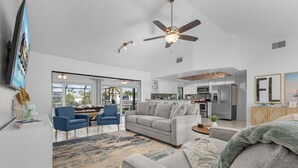 A spacious living area with a grey sofa, blue armchairs, and a dining table. A ceiling fan and recessed lighting are visible. - Waterfront Living, Dock, Heated Pool & Spa - Gulf Gate Oasis - Roelens (Cape Coral)