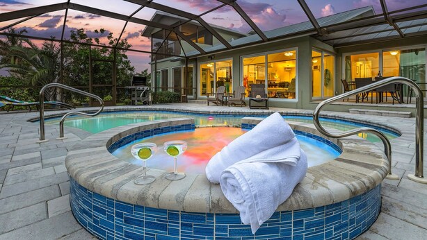A hot tub with a glass enclosure, surrounded by a patio area with chairs and a table. - Waterfront Living, Dock, Heated Pool & Spa - Gulf Gate Oasis - Roelens (Cape Coral)