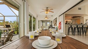 A spacious dining area with a wooden table set for a meal, large windows, and a view of the outdoors. - Waterfront Living, Dock, Heated Pool & Spa - Gulf Gate Oasis - Roelens (Cape Coral)