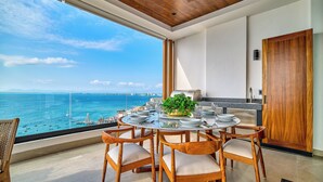A dining area with a view of the ocean and a bridge, wooden chairs, a table set for four, and a potted plant. - Chic Penthouse Ocean Views, Rooftop Pool & Balcony (Puerto Vallarta)