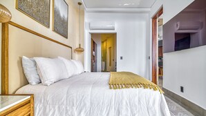 A bedroom with a large bed, a bedside table, and a wooden headboard. There is a hallway leading to other rooms. - Chic Penthouse Ocean Views, Rooftop Pool & Balcony (Puerto Vallarta)