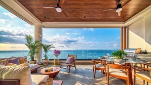A spacious outdoor area with a wooden ceiling, a dining table set for two, and a view of the ocean. - Chic Penthouse Ocean Views, Rooftop Pool & Balcony (Puerto Vallarta)