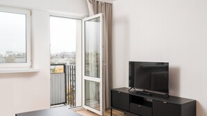 A modern living room with a sliding glass door leading to a balcony, a black entertainment unit, and a large window. - Elbląska Modern Apartment (Warszawa)