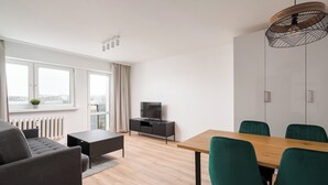 A modern living room with a sofa, a coffee table, a TV, and a dining area with chairs and a table. - Elbląska Modern Apartment (Warszawa)
