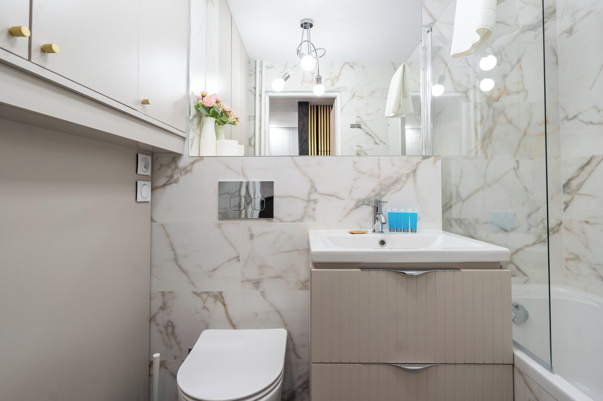 Un baño moderno con salpicadero de mármol, un lavamanos blanco, un inodoro y una zona de ducha.