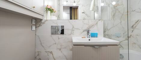 Un baño moderno con salpicadero de mármol, un lavamanos blanco, un inodoro y una zona de ducha.