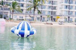 A large inflatable blue and white beach ball floating in calm water, with a hotel and palm trees in the background. - Angel Garden Resort Coron (Busuanga)