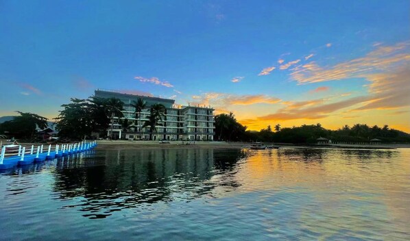 A hotel with a large building, a dock with boats, and a calm lake reflecting the sky. - Angel Garden Resort Coron (Busuanga)