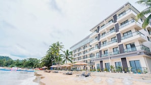 A beachfront hotel with multiple balconies, a sandy beach, and palm trees. - Angel Garden Resort Coron (Busuanga)