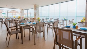 A spacious dining area with multiple tables and chairs, large windows offering a view of the sea, and potted plants on the tables. - Angel Garden Resort Coron (Busuanga)