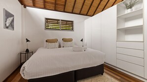 A bedroom with a bed, bedside lamps, a window with blinds, a wall-mounted shelf, and a framed picture.