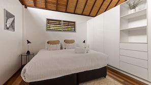 Ein Schlafzimmer mit einem Bett, Nachttischlampen, einem Fenster mit Jalousien, einem Wandregal und einem gerahmten Bild.